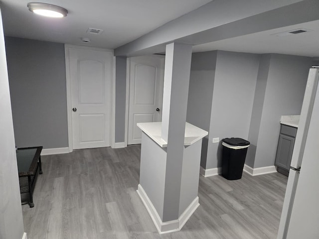 finished below grade area featuring light wood-style floors, baseboards, freestanding refrigerator, and visible vents