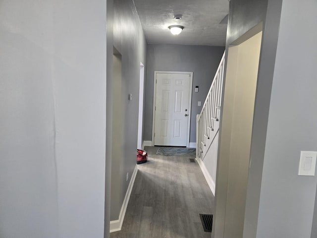 hallway featuring baseboards, visible vents, wood finished floors, and stairway