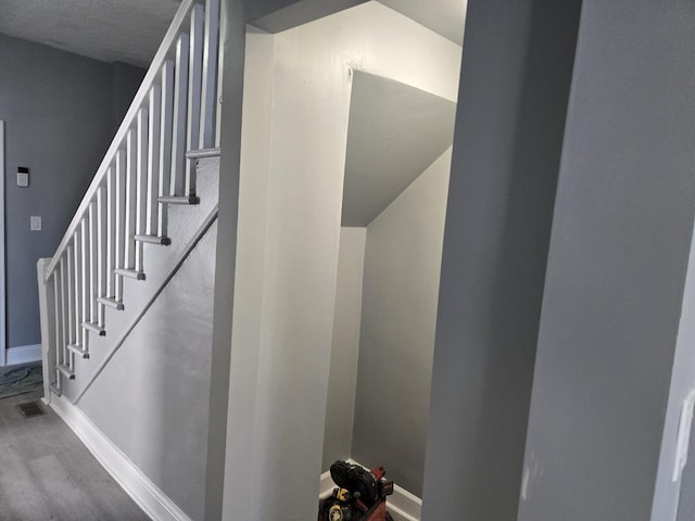 staircase with baseboards, visible vents, and wood finished floors