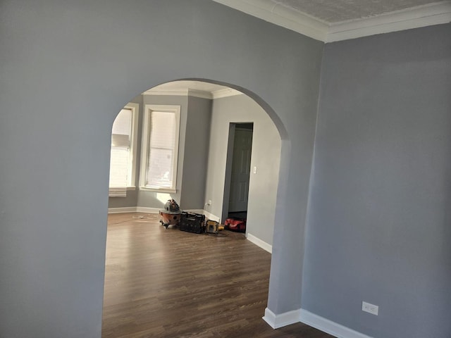 empty room featuring baseboards, ornamental molding, arched walkways, and wood finished floors