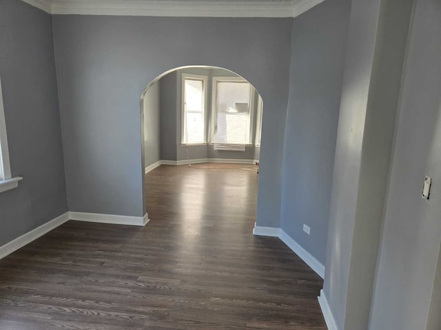 empty room featuring arched walkways, baseboards, dark wood finished floors, and ornamental molding