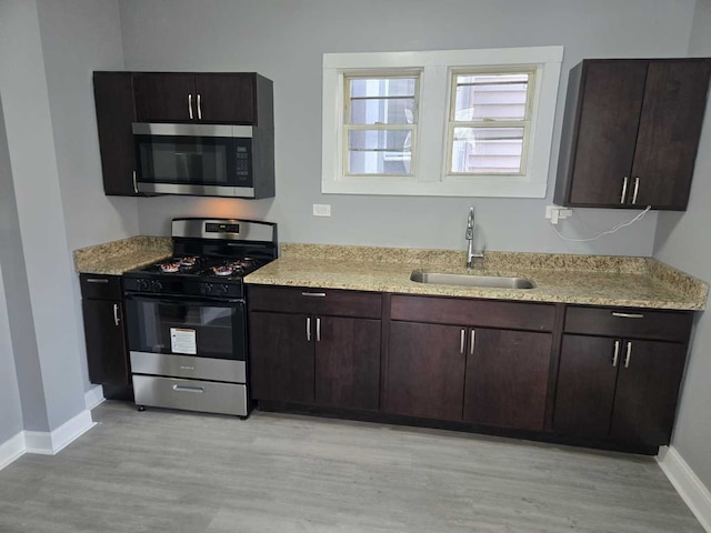 kitchen featuring dark brown cabinetry, a sink, baseboards, stainless steel appliances, and light wood-style flooring