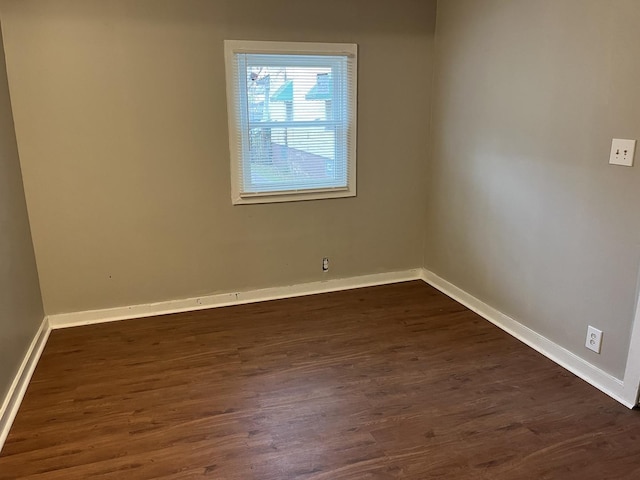 spare room featuring baseboards and dark wood-type flooring