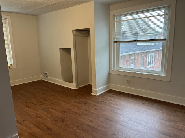 unfurnished bedroom featuring baseboards, dark wood-style flooring, a textured ceiling, and visible vents