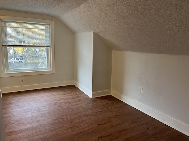 additional living space with baseboards, a textured ceiling, lofted ceiling, and dark wood finished floors