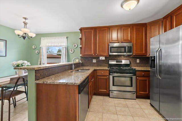 kitchen with appliances with stainless steel finishes, a sink, a peninsula, stone counters, and tasteful backsplash
