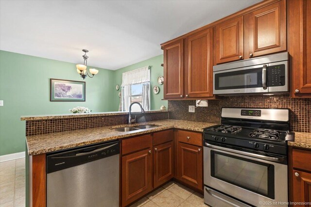 kitchen with a peninsula, light tile patterned flooring, tasteful backsplash, a sink, and appliances with stainless steel finishes