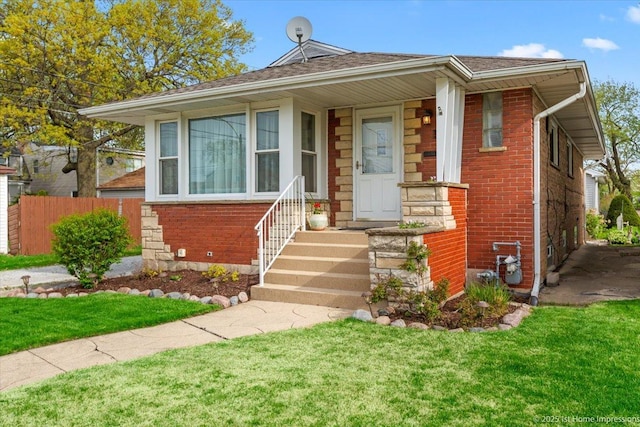 bungalow-style house with fence, a shingled roof, a front yard, and brick siding
