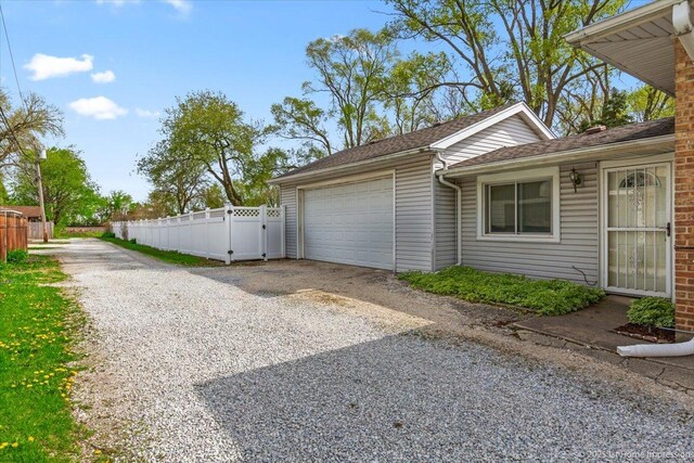 view of home's exterior with gravel driveway, fence, a gate, and a garage