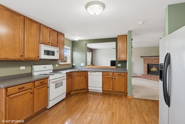 kitchen featuring a sink, a fireplace, white appliances, brown cabinetry, and light wood-style flooring