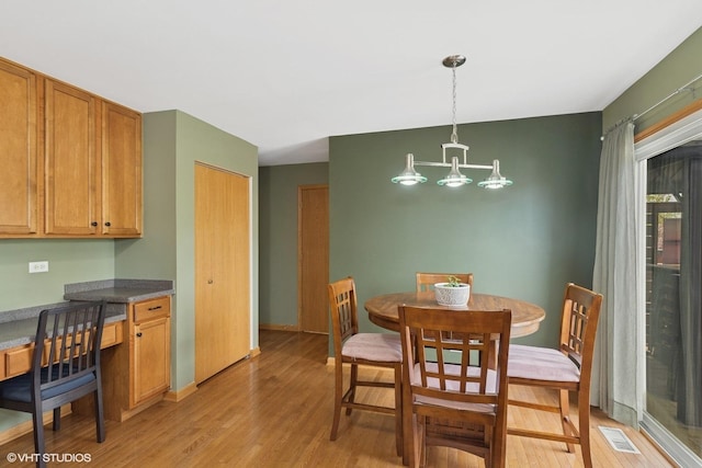 dining space with a notable chandelier, visible vents, built in study area, and light wood-type flooring