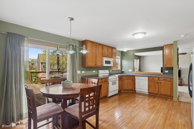 kitchen with dark countertops, a sink, light wood-style floors, white appliances, and brown cabinetry