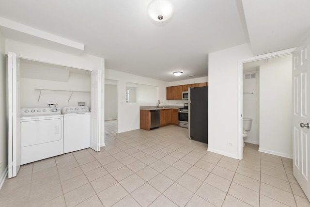 interior space with visible vents, washer and dryer, light tile patterned flooring, brown cabinets, and stainless steel appliances