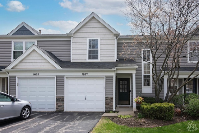 view of property featuring driveway, stone siding, and a garage