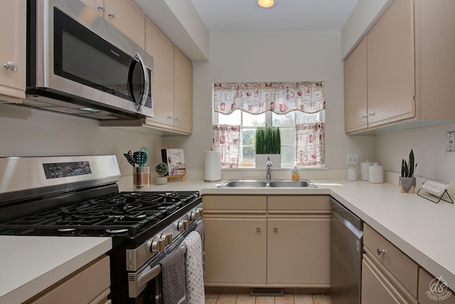 kitchen with a sink, appliances with stainless steel finishes, cream cabinets, and light countertops