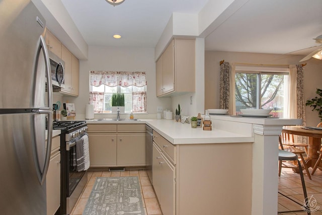 kitchen with appliances with stainless steel finishes, cream cabinets, a peninsula, and a wealth of natural light