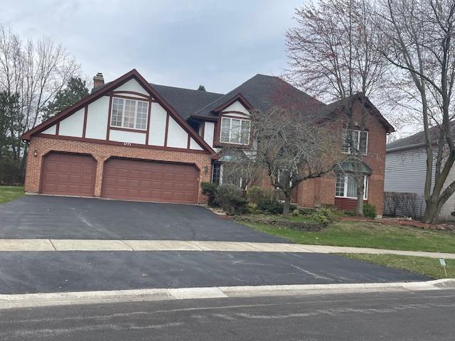 tudor home featuring brick siding, a garage, aphalt driveway, and a chimney