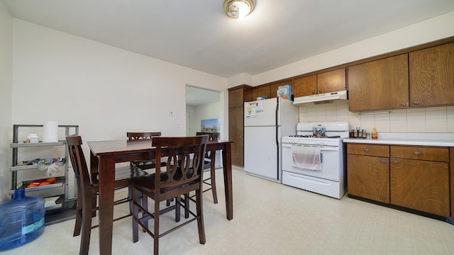 kitchen with white appliances, light countertops, under cabinet range hood, brown cabinets, and backsplash