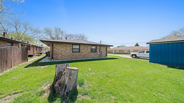 rear view of house with a yard, brick siding, and fence