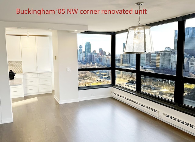 unfurnished dining area with a city view, baseboards, a baseboard heating unit, and wood finished floors
