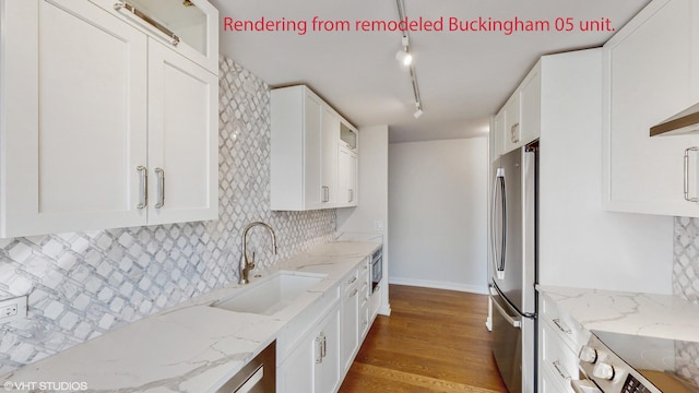 kitchen with decorative backsplash, wood finished floors, white cabinets, a sink, and stainless steel appliances