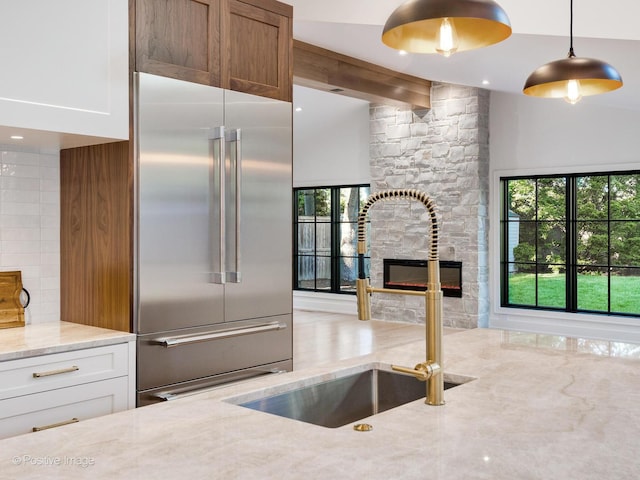 118 Lockerbie Ln, Wilmette, IL 60091 - kitchen with built in fridge, a sink, light stone counters, a stone fireplace, and white cabinetry