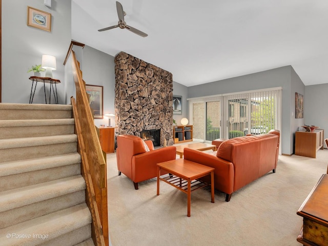 living area featuring ceiling fan, light colored carpet, a stone fireplace, stairs, and lofted ceiling