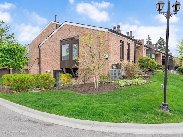 view of home's exterior featuring a lawn, a chimney, central AC, and brick siding