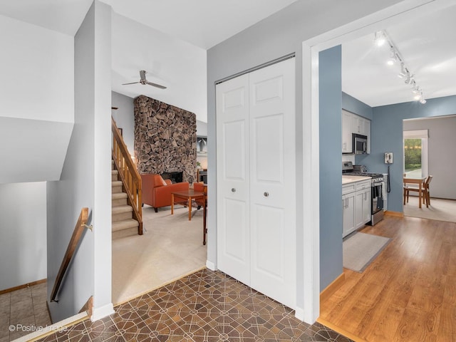 interior space featuring ceiling fan, a stone fireplace, appliances with stainless steel finishes, rail lighting, and light countertops