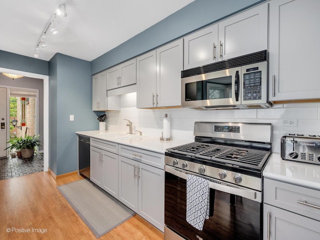 kitchen featuring appliances with stainless steel finishes, tasteful backsplash, a sink, light countertops, and light wood finished floors