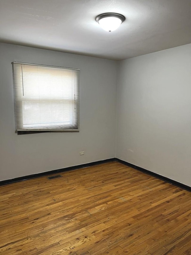 spare room with baseboards, wood finished floors, and visible vents