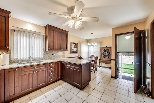 kitchen featuring decorative backsplash, a peninsula, light stone countertops, a sink, and ceiling fan with notable chandelier