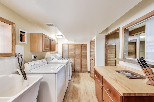 clothes washing area featuring cabinet space, a sink, light wood-type flooring, visible vents, and washing machine and dryer