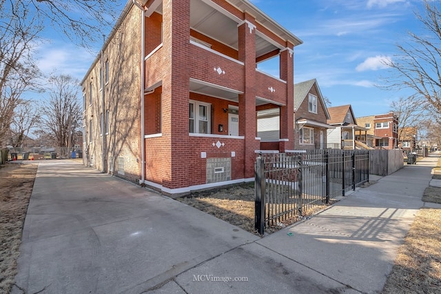 view of home's exterior featuring covered porch, brick siding, concrete driveway, a fenced front yard, and a residential view