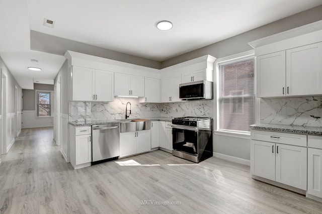 kitchen with decorative backsplash, appliances with stainless steel finishes, a sink, light stone counters, and white cabinetry