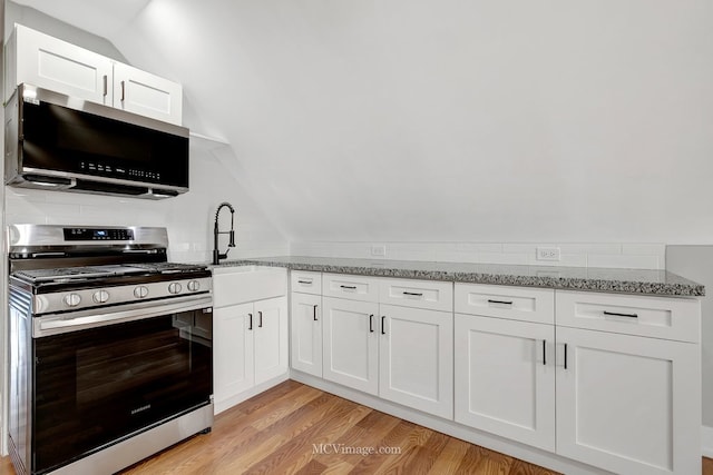 kitchen with light stone counters, light wood finished floors, appliances with stainless steel finishes, and vaulted ceiling