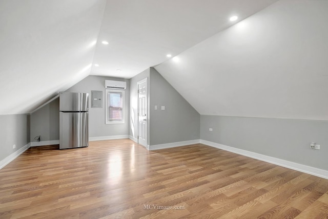 bonus room featuring light wood-style floors, baseboards, vaulted ceiling, a wall mounted AC, and electric panel