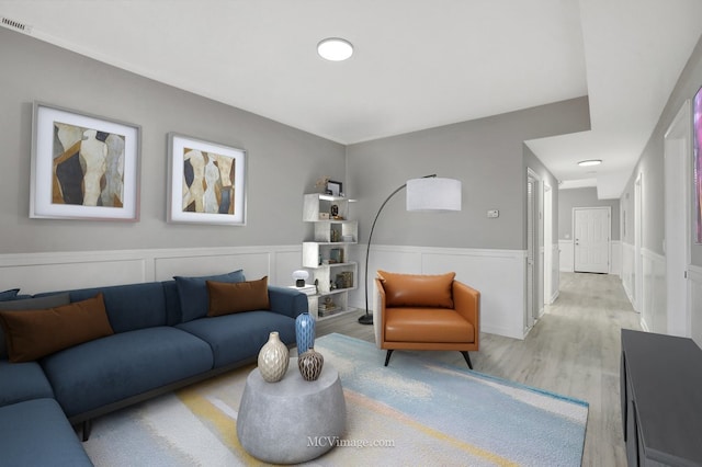 living room featuring a decorative wall, wainscoting, wood finished floors, and visible vents