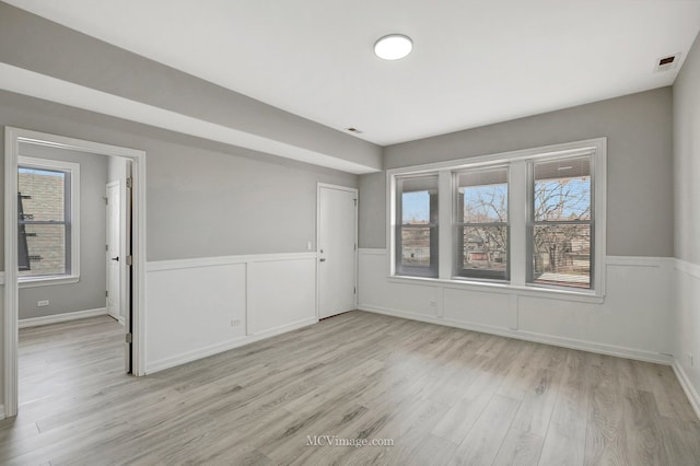 unfurnished room featuring light wood-style floors and a wainscoted wall