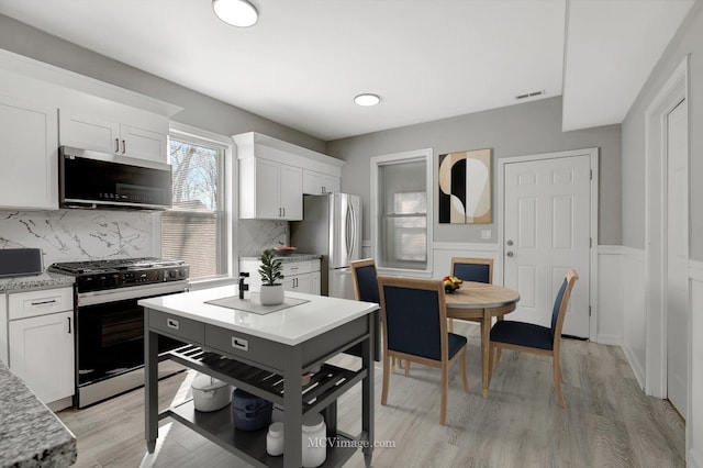 kitchen featuring decorative backsplash, visible vents, freestanding refrigerator, range with gas stovetop, and white cabinetry