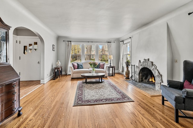 living area featuring light wood-style floors, arched walkways, a fireplace, and a wealth of natural light