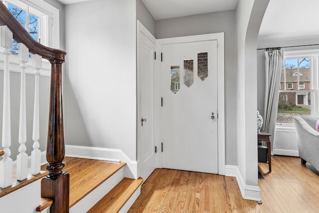 foyer with stairs, arched walkways, and light wood finished floors