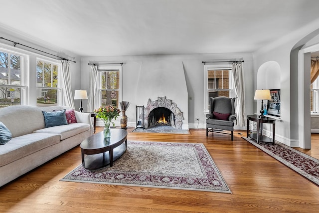 living room featuring a large fireplace, baseboards, arched walkways, and wood finished floors