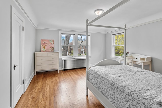 bedroom featuring radiator, ornamental molding, wood-type flooring, and baseboards