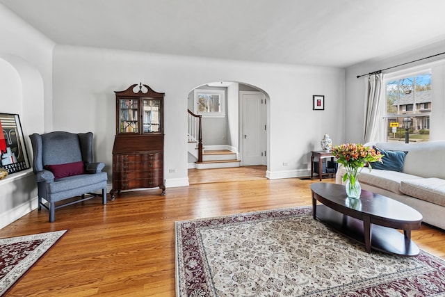 living area with stairs, arched walkways, baseboards, and light wood finished floors