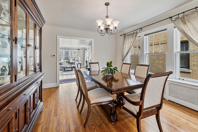dining area with baseboards, a notable chandelier, radiator heating unit, and light wood finished floors