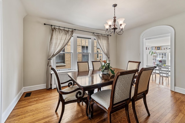 dining space with baseboards, a notable chandelier, light wood-style flooring, and visible vents