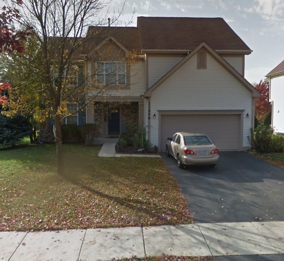 view of front of property featuring a garage, aphalt driveway, stone siding, and a front yard