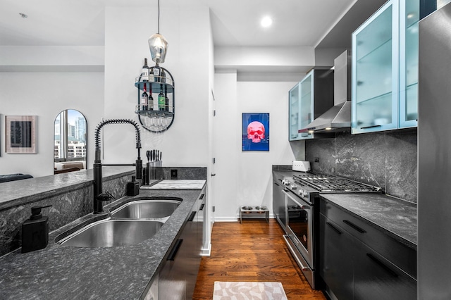 kitchen with dark wood-type flooring, wall chimney exhaust hood, a sink, dark stone countertops, and stainless steel appliances