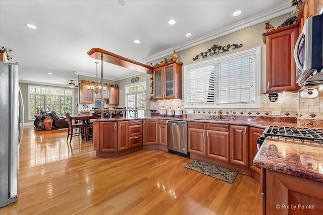kitchen featuring crown molding, appliances with stainless steel finishes, a sink, a peninsula, and light wood-type flooring